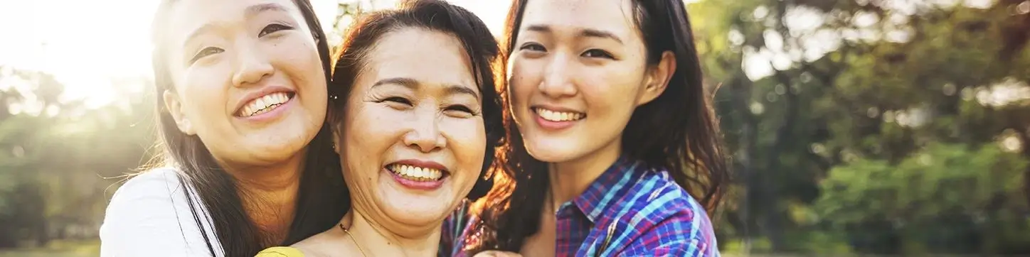 Three smiling women from different generations of one family standing together outdoors